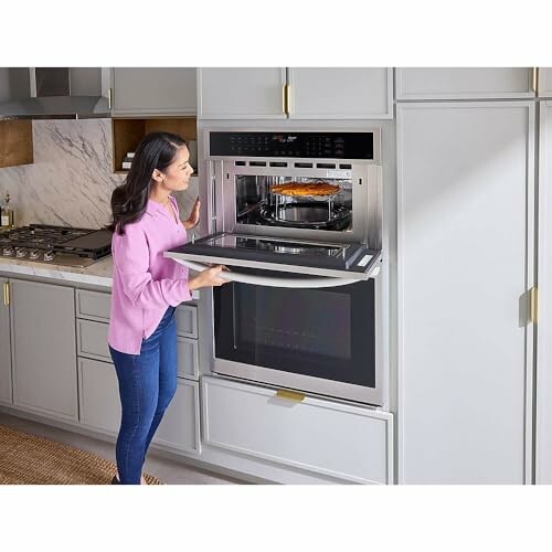 Woman opening a built-in oven in a modern kitchen.